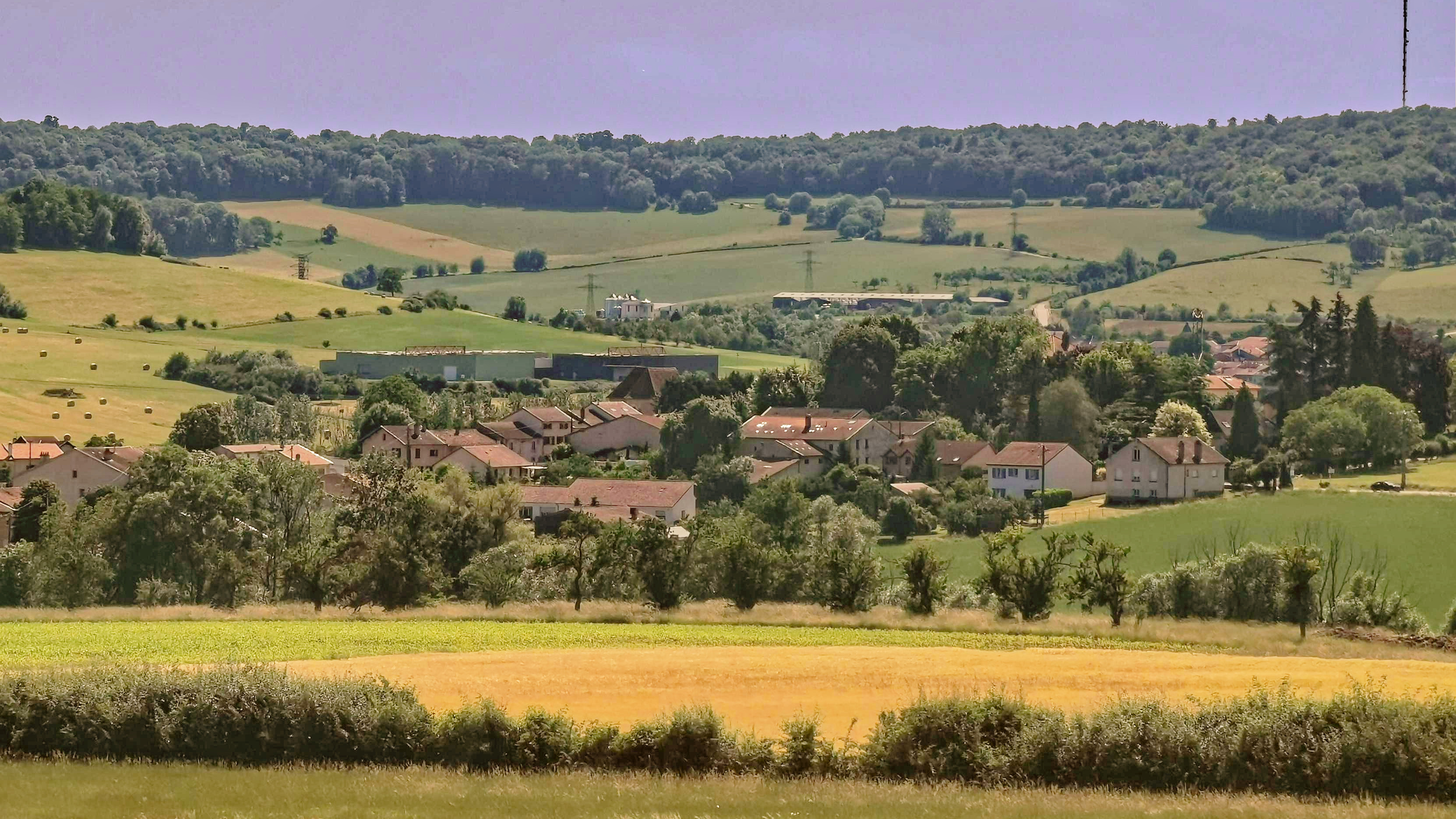 Un paysage. Beaucoup de verdure. Un village se dessine à peu près au centre.